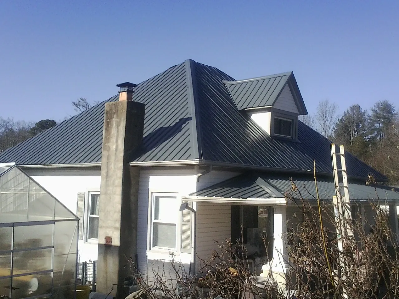 Dark blue standing seam metal roof on a white farmhouse with dormer — Slate & Tile Roof Repair by Roofing Brothers in Gray Summit