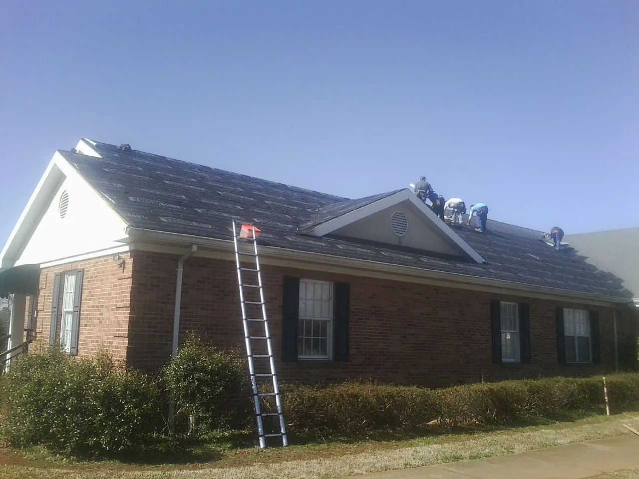 Crew tearing shingles off a brick ranch roof with a ladder set — Metal Roof Repair work by our crew in Gray Summit