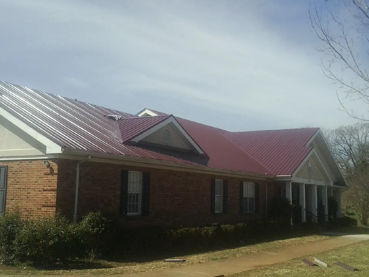 Red metal roof with gabled entries on a long brick building, from a Hail Damage Roof Repair job in Gray Summit