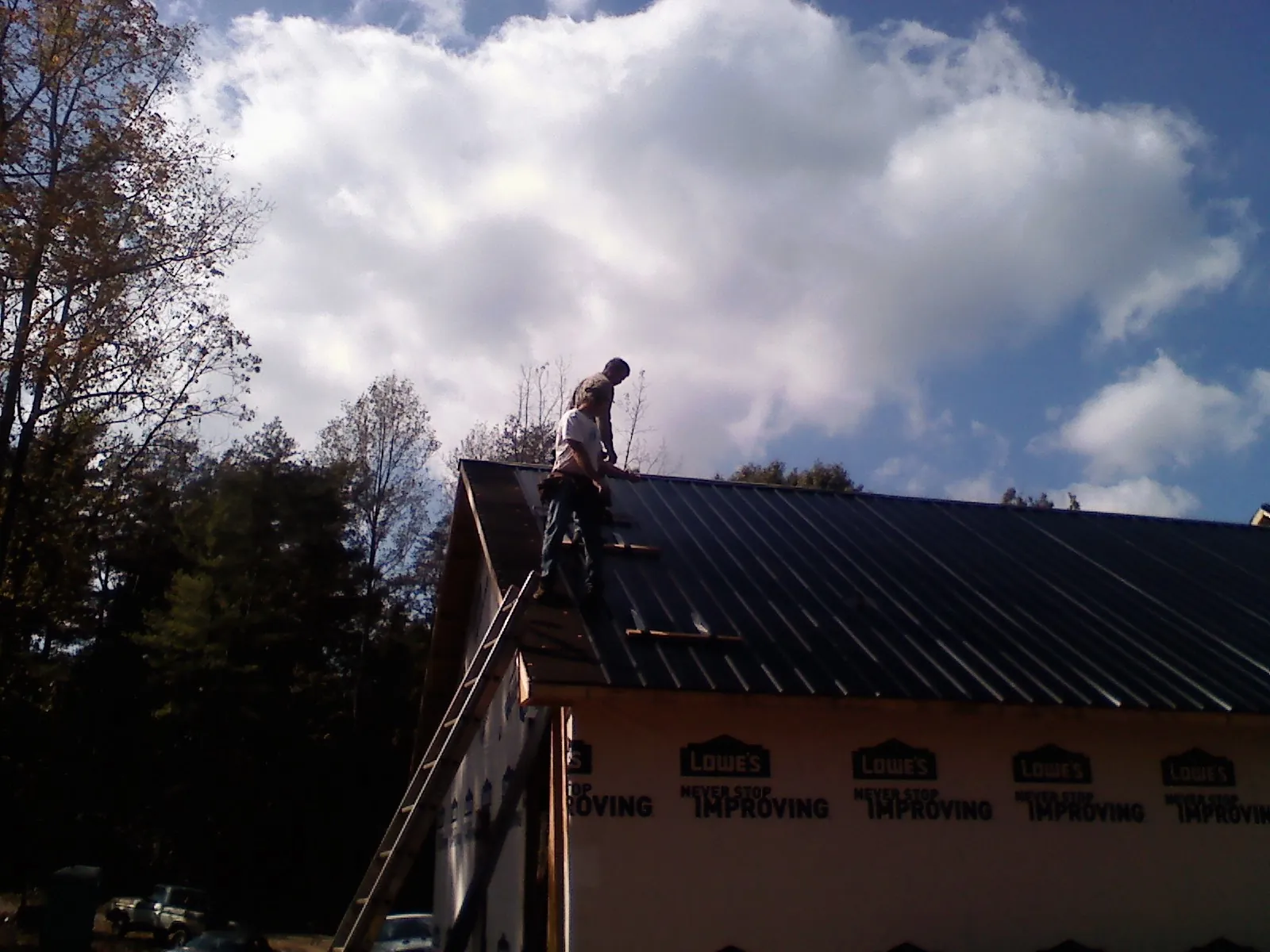 Roofer fastening dark metal panels high against a cloudy sky, from a Roof Inspection job in Gray Summit