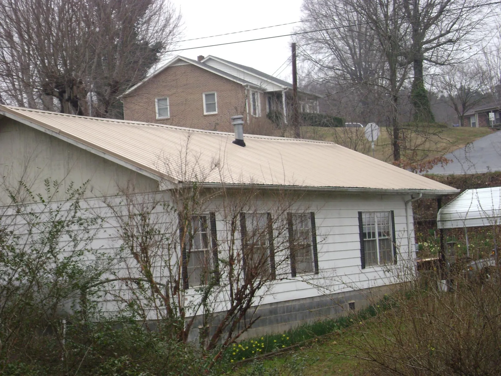 Tan metal roof on a white sided house set into a hillside — Commercial Roofing by Roofing Brothers in Gray Summit